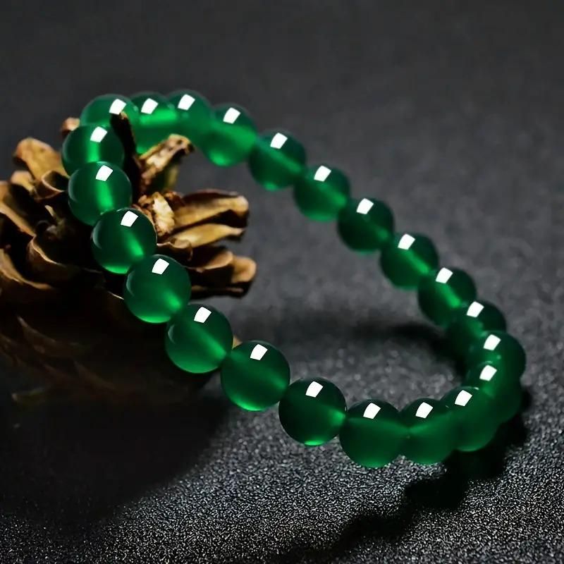 Green beaded bracelet on a dark surface with a pine cone