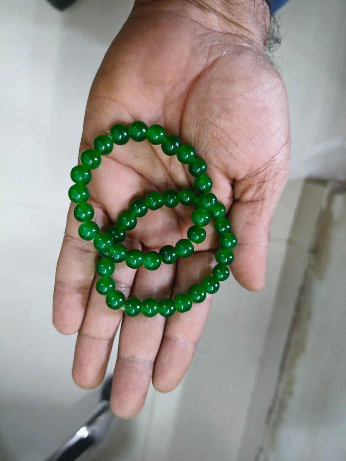 Hand holding two green beaded bracelets against a neutral background
