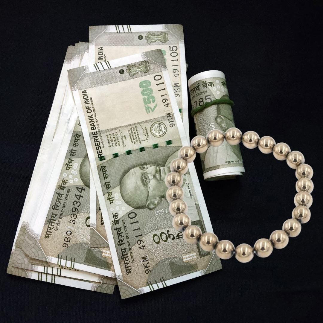 Pyrite Bead Bracelet with Indian currency notes and a pearl necklace on a black background